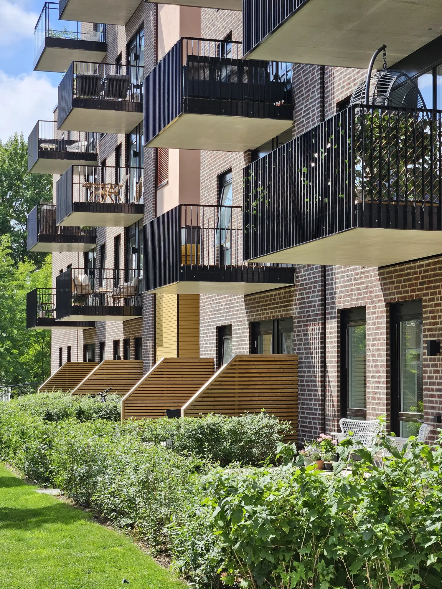 Lille Løren park, teglfasader med innslag av puss i ulike farger, og trekledning. Oppbrutte volumer, og grønne og frodige utearealer.