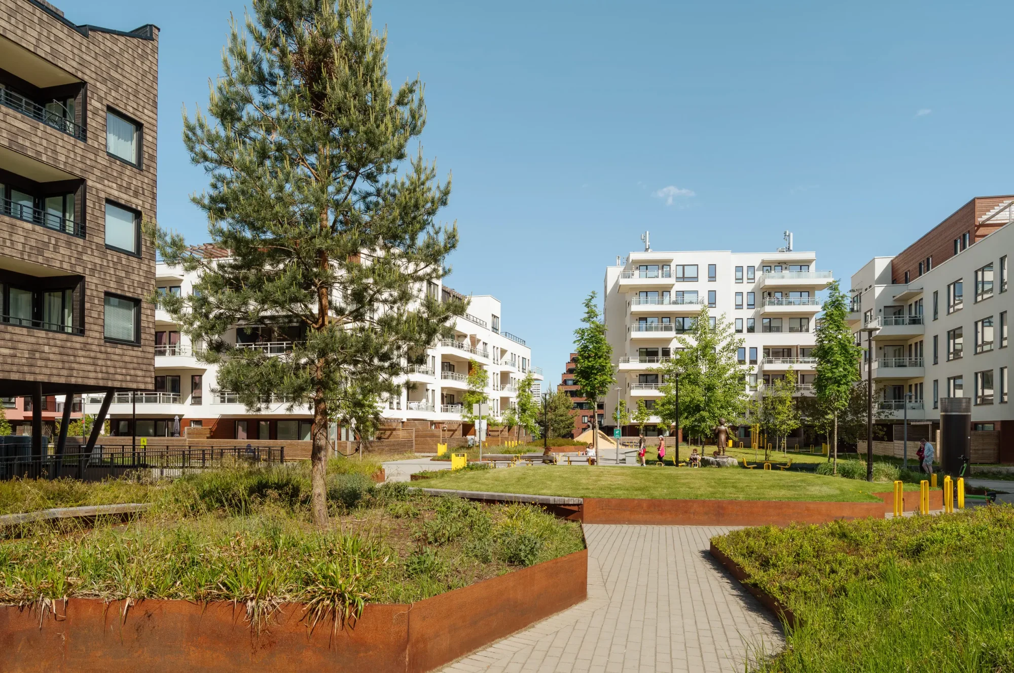 Skårerbyen. Fasadene har hvit puss, farget balkongrekkverk, og farget beslag på dekkeforkanter, slik at balkongene i større grad er en del av fasadelivet, og gir et skulpturelt uttrykk. Utearealet er grønt og frodig. Kongla skiller seg ut med mørk brun skjermtegl.