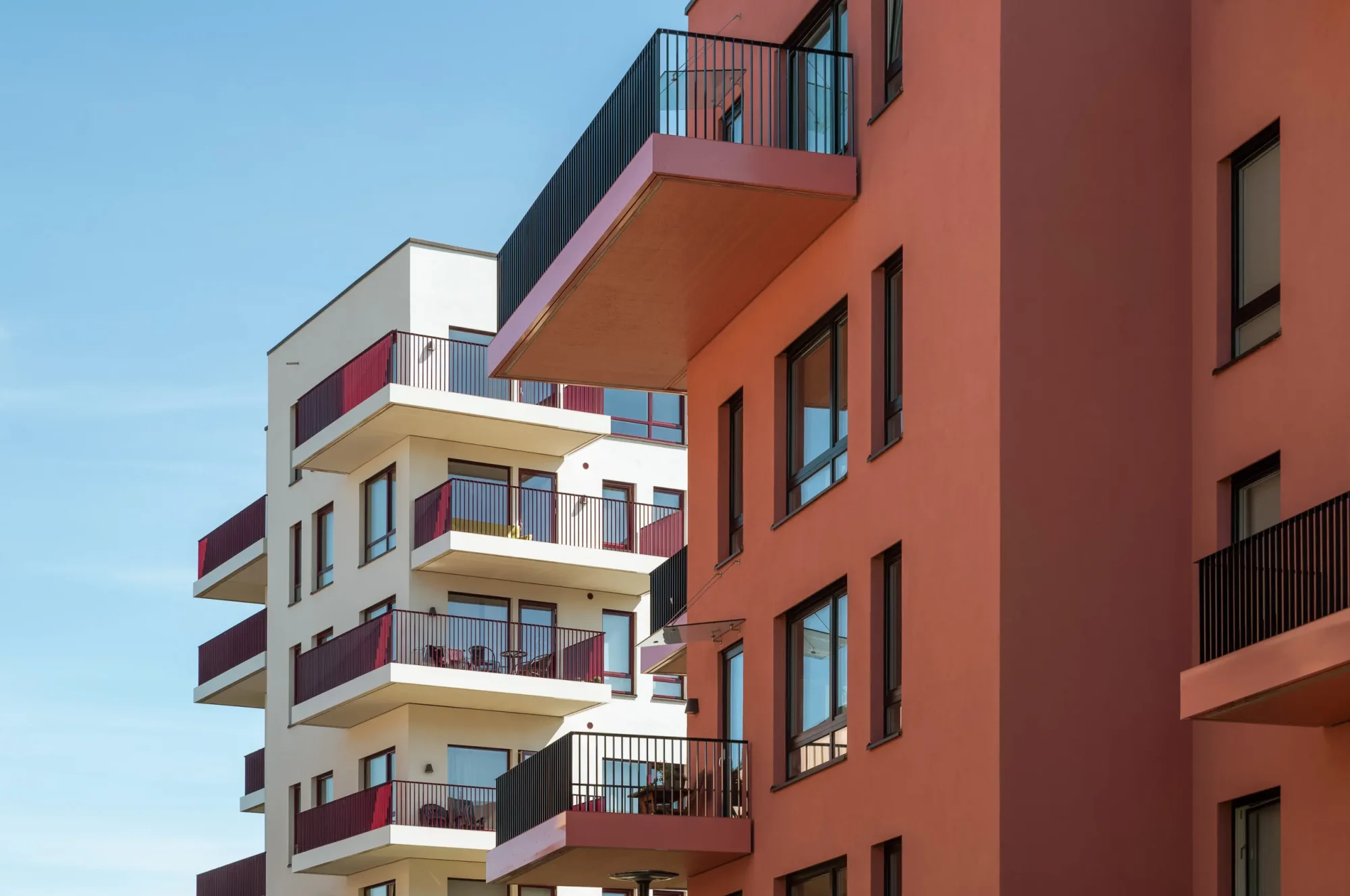 Gårdskvartalet med barnehage på Skårer skårerbyen. fasadene har rød/ rosa puss, farget balkongrekkverk, og farget beslag på dekkeforkanter, slik at balkongene i større grad er en del av fasadelivet, og gir et skulpturelt uttrykk.