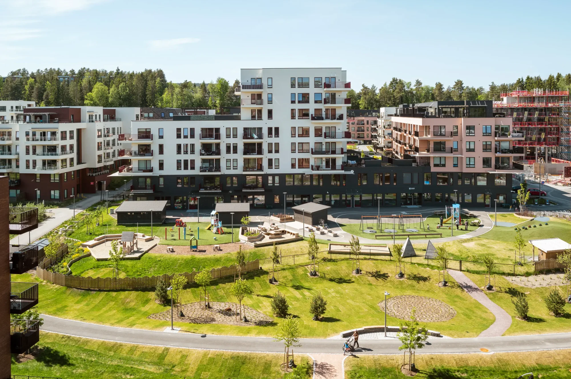 Gårdskvartalet med barnehage på Skårer skårerbyen. fasadene har hvit og rød/ rosa puss, farget balkongrekkverk, og farget beslag på dekkeforkanter, slik at balkongene i større grad er en del av fasadelivet, og gir et skulpturelt uttrykk. Utearealet er grønt og frodig.